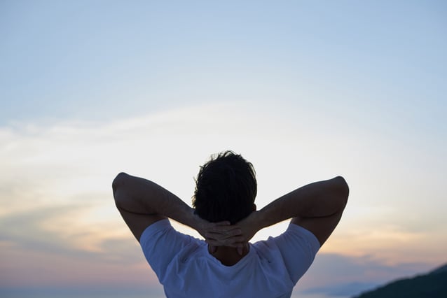 handsome young man relaxing and working on laptop computer at home balcony while looking sunset