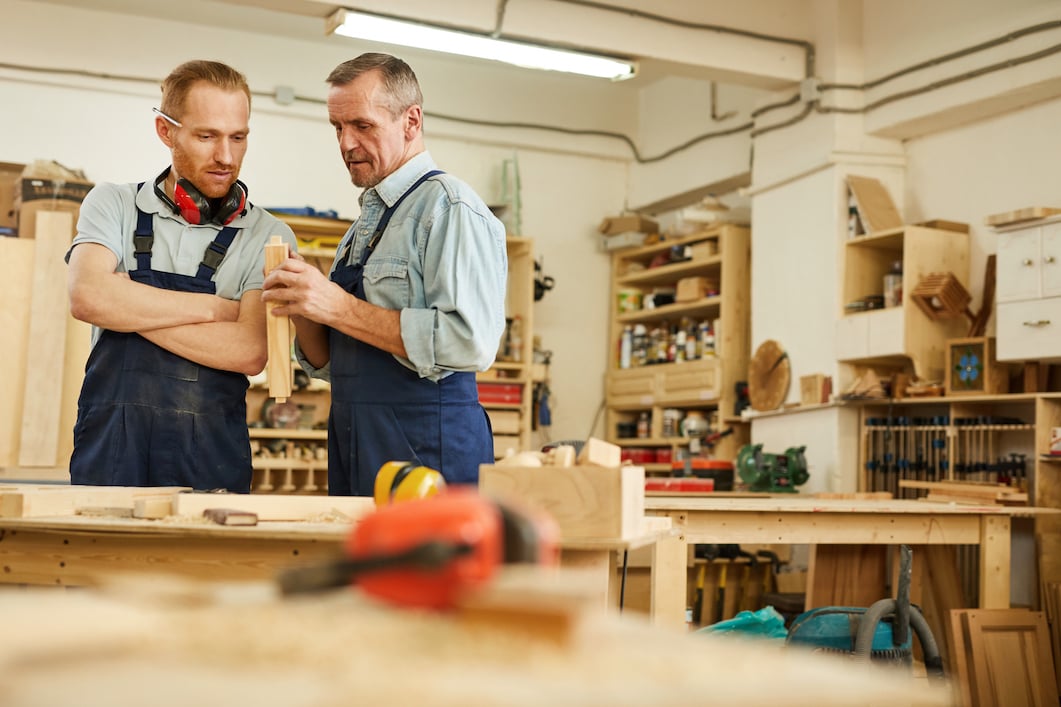 Two men talking over a workbench in a woodshop